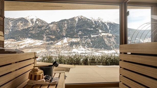 A wooden bench with a view of snow-covered mountains through a large window. - Apartments VIU - 01 Cozy VIU (Bad Hofgastein)
