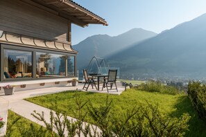 A modern building with large windows, a patio with a table and chairs, and a view of mountains. - Apartments VIU - 01 Cozy VIU (Bad Hofgastein)