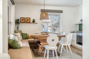 A modern kitchen with a dining area, wooden table, white chairs, and a hanging light fixture.