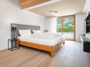 Ein modernes Schlafzimmer mit einem Holzbett, einem Nachttisch, einer Lampe und einem großen Fenster mit Blick auf Grünflächen.