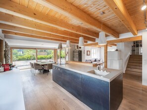 A modern kitchen with a large island, wooden beams, and pendant lighting.