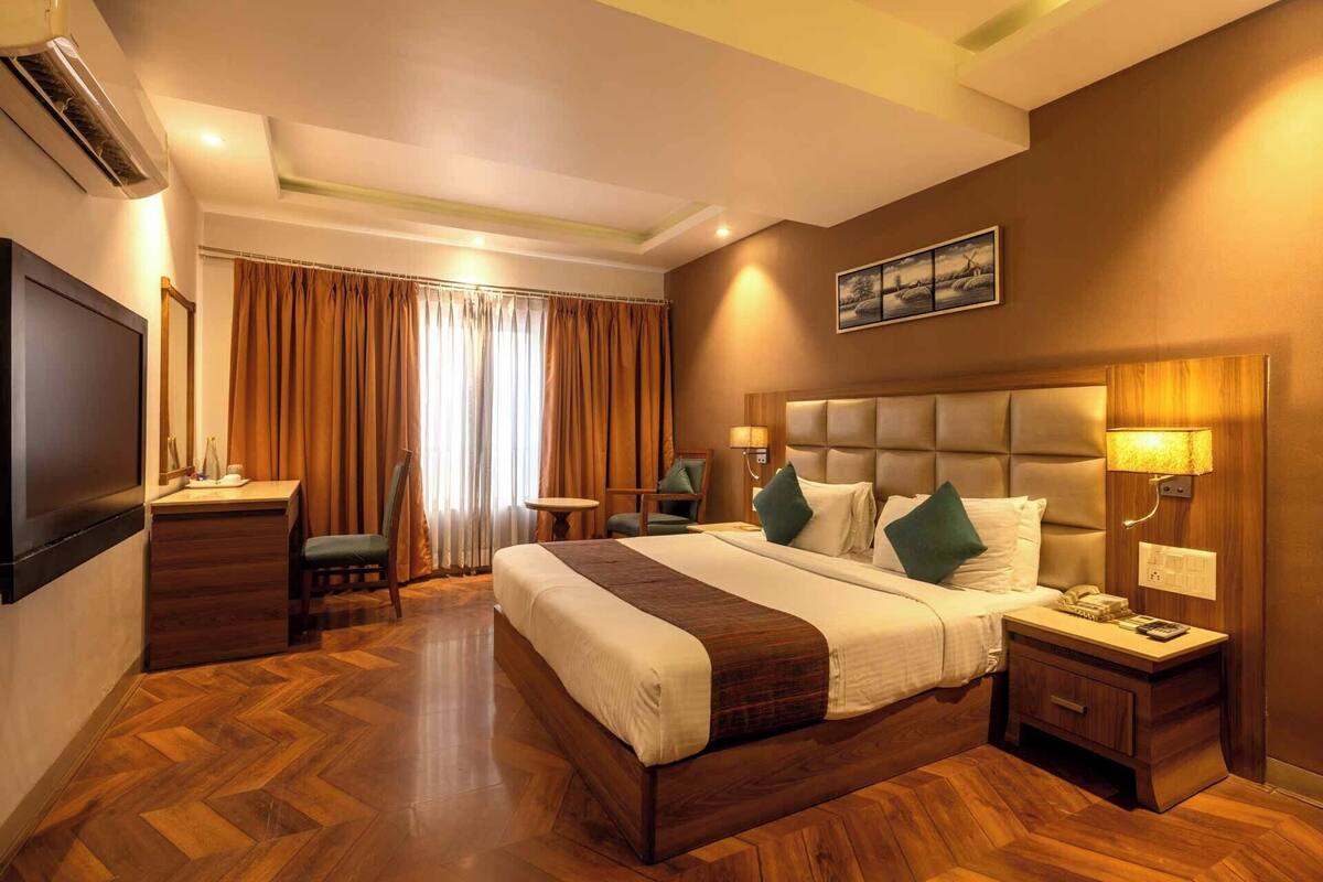 A hotel room with a bed, bedside table, lamp, chair, and a television.