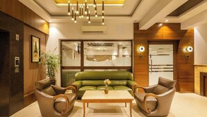 En moderne lobby med en grøn sofa, to læderlænestole, et træbord og en lysekrone.