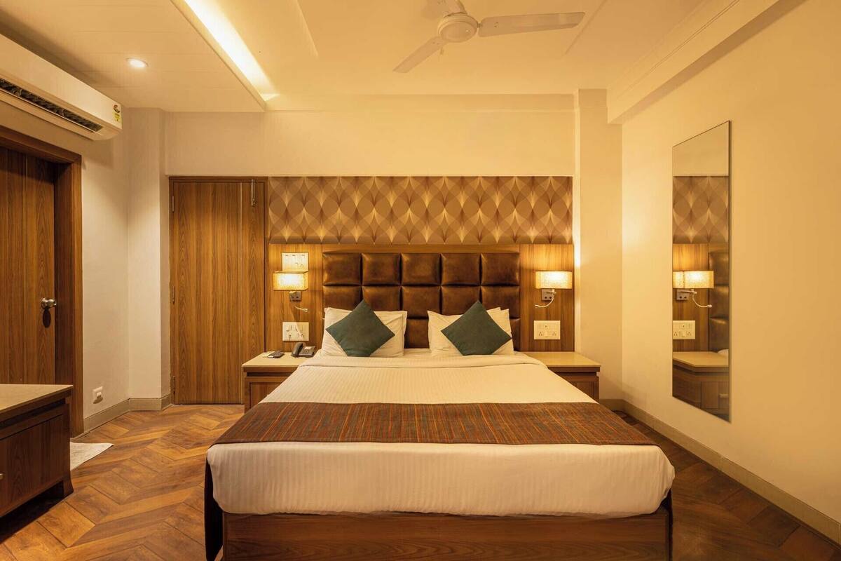 A hotel room with a large bed, wooden headboard, two bedside tables with lamps, a ceiling fan, and a wooden wardrobe.