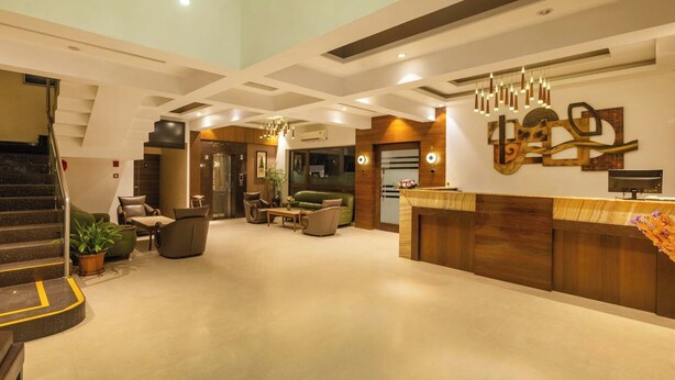 En rummelig lobby med trappe, siddeområde, receptionsdisk og en moderne lysekrone.