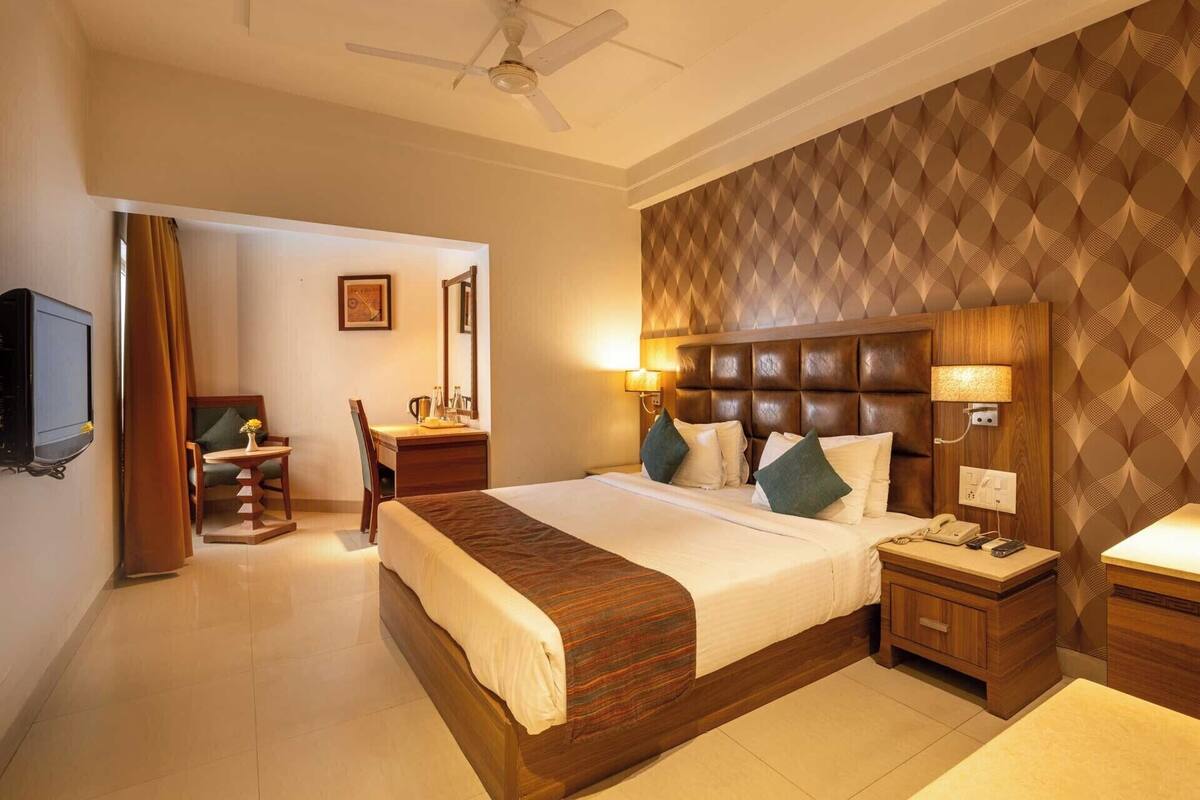 A hotel room with a bed, bedside table, lamp, and a television.