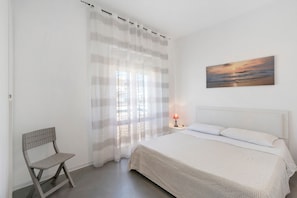 Un dormitorio con cama, una silla, un cuadro y una lámpara.