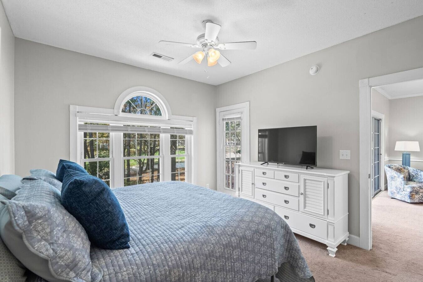 Un dormitorio con cama, televisor, cómoda y ventana con vista a árboles.