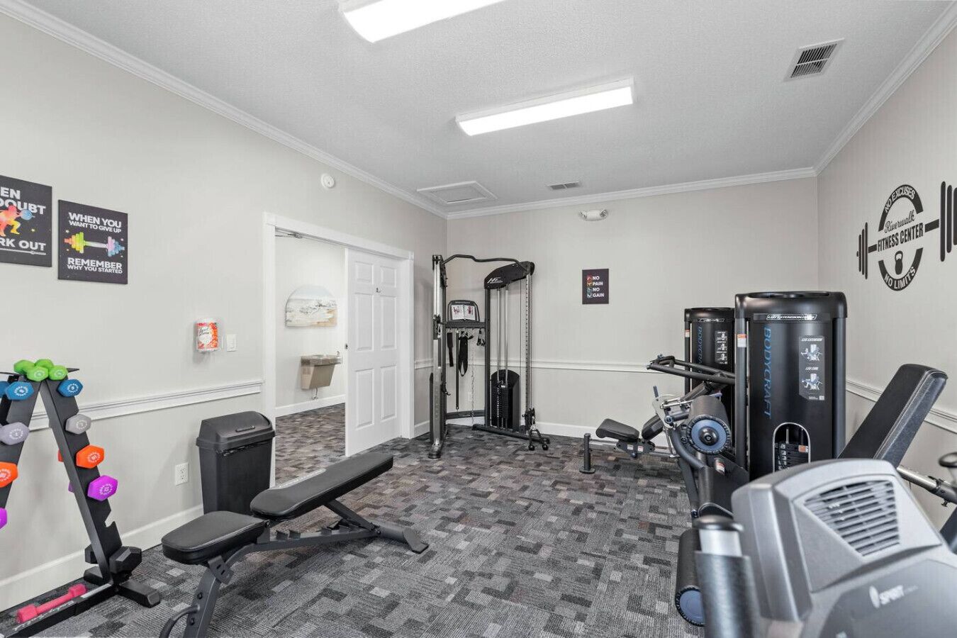 Une salle de sport équipée de matériel d’exercice, d’un banc et ornée d’affiches motivantes.