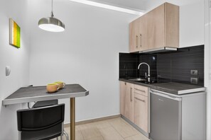 Una cocina compacta de diseño moderno, con un lavamanos negro, armarios de madera y una pequeña mesa de comedor con sillas.