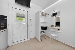 A room with a white door, a mounted television, a towel rack, a small stool, and a shelf with a microwave and a potted plant. - Studio Apartment 'Sivota Colours 23' with Private Terrace, Wi-Fi and Air Conditioning (Sivota)