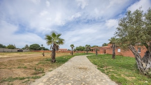 Un chemin pavé mène à un bâtiment à la façade rouge, entouré de verdure et de palmiers.