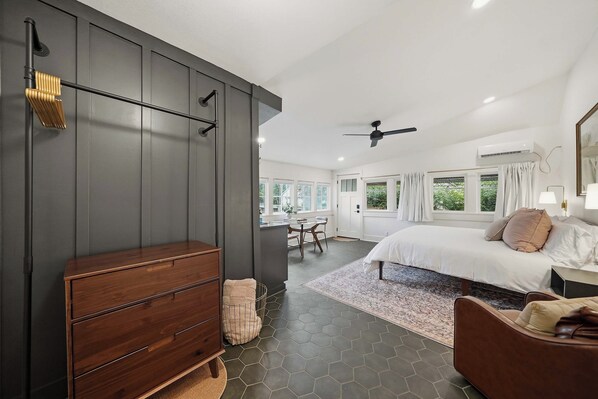 A modern bedroom with a large bed, a wooden dresser, and a view of the dining area.