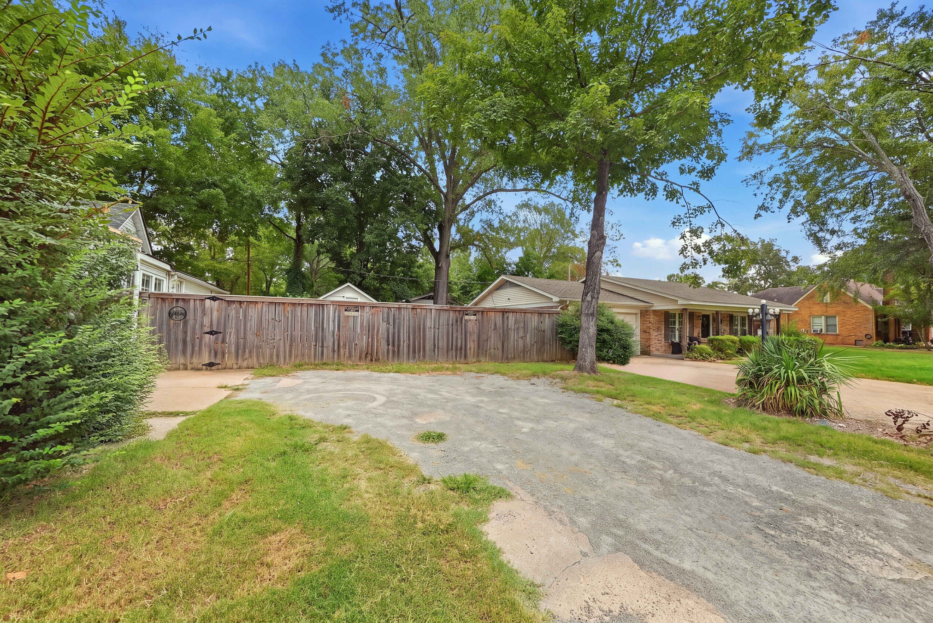 A residential area with a fenced backyard, a driveway, and houses with brick exteriors.