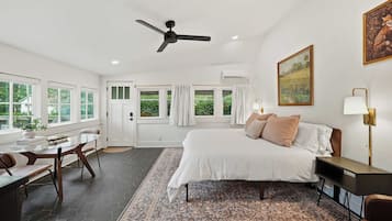 Quarto de hotel com cama, escrivaninha, cadeira, ventoinha no teto e um quadro na parede.