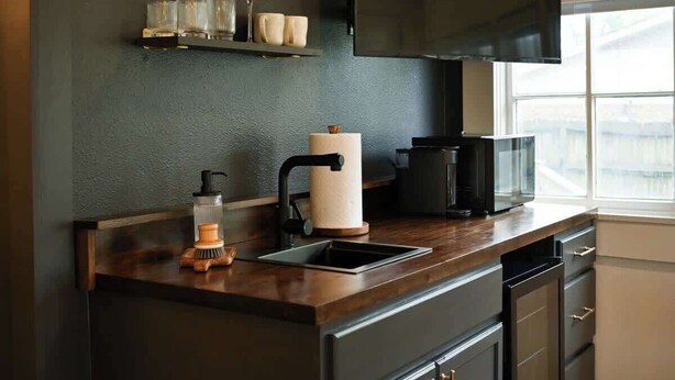 A modern kitchen with dark cabinetry, a flat-screen TV, a microwave, and a window providing natural light.