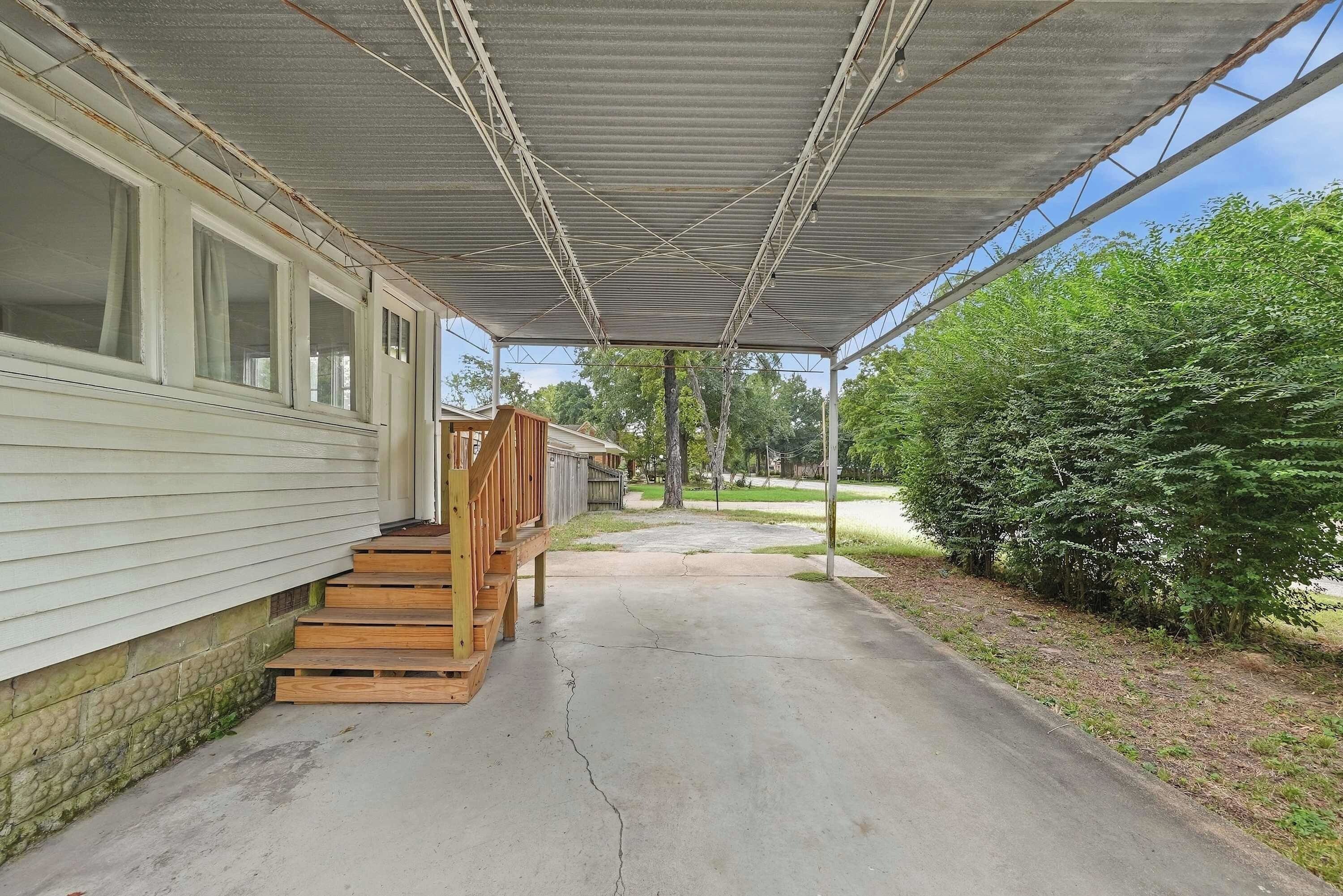 A covered porch with a wooden deck leading to a house with a garage.