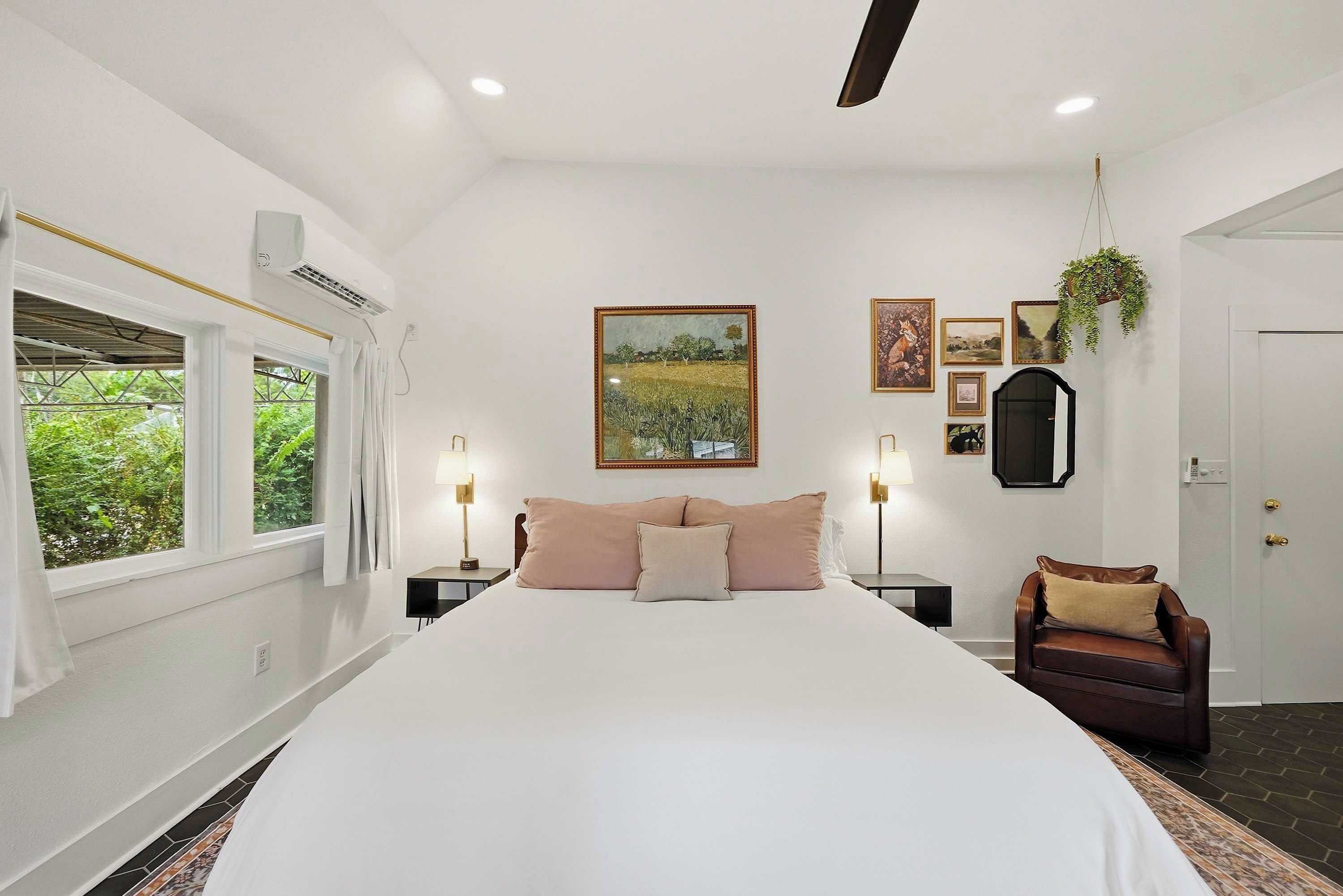 A bedroom with a large bed, bedside tables, a hanging plant, and artwork on the walls.