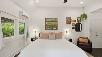 A bedroom with a large bed, bedside tables, a hanging plant, and artwork on the walls.