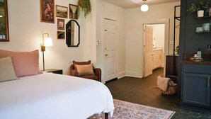 A bedroom with a large bed, a nightstand, a chair, a mirror, and a door leading to a bathroom.