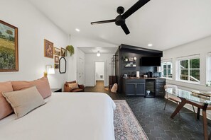 Un dormitorio moderno con una cama grande, una zona de estar con sofá y una cocina con mesa de comedor.