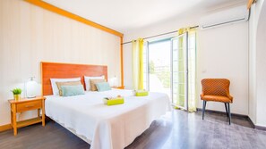 Ein Hotelzimmer mit einem großen Bett, einem Nachttisch, einem Sessel und einem Fenster mit Vorhängen.
