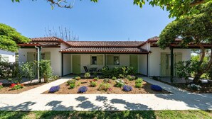 Un bâtiment à deux étages, doté d’un toit recouvert de tuiles, d’un jardin devant avec différentes plantes et d’un chemin pavé.