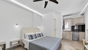 Une chambre à coucher comprenant un lit, des tables de chevet, un ventilateur de plafond et une kitchenette équipée d’un lave-vaisselle.