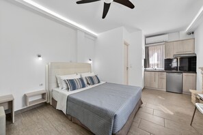 Un dormitorio con cama, mesitas de noche, ventilador de techo y una kitchenette con lavavajillas.