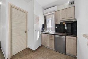 Eine kleine Küche mit Geschirrspüler, Holzschränken, einem Fenster mit Vorhängen und einer Lampe.