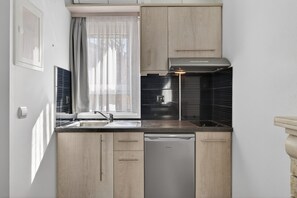 Una cocina compacta con lavavajillas, ventana con cortinas translúcidas y salpicadero negro.