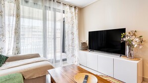 Ett modernt vardagsrum med en soffa, ett soffbord i trä, en tv på ett vitt skåp och ett fönster med blommiga gardiner.