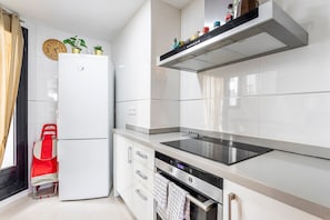 A modern kitchen with white cabinets, a stainless steel range hood, a built-in oven, and a refrigerator.