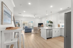 A modern kitchen with white cabinetry, a central island, and a dining area with a blue sofa. - New 4bedroom house walking distance to the beach (Myrtle Beach)