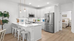 Une cuisine moderne avec des meubles blancs, des appareils en acier inoxydable et un îlot central doté de tabourets.