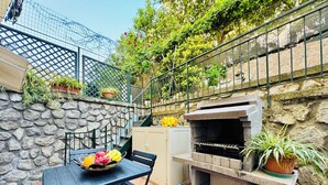 An outdoor patio with a stone wall, a grill, a table with chairs, and potted plants. - YourHome - Letizia's House (Sorrento)