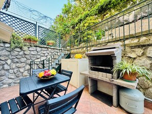 Eine Terrass mit Steinwand, Grill, Tisch und Stühlen sowie Kübelpflanzen.
