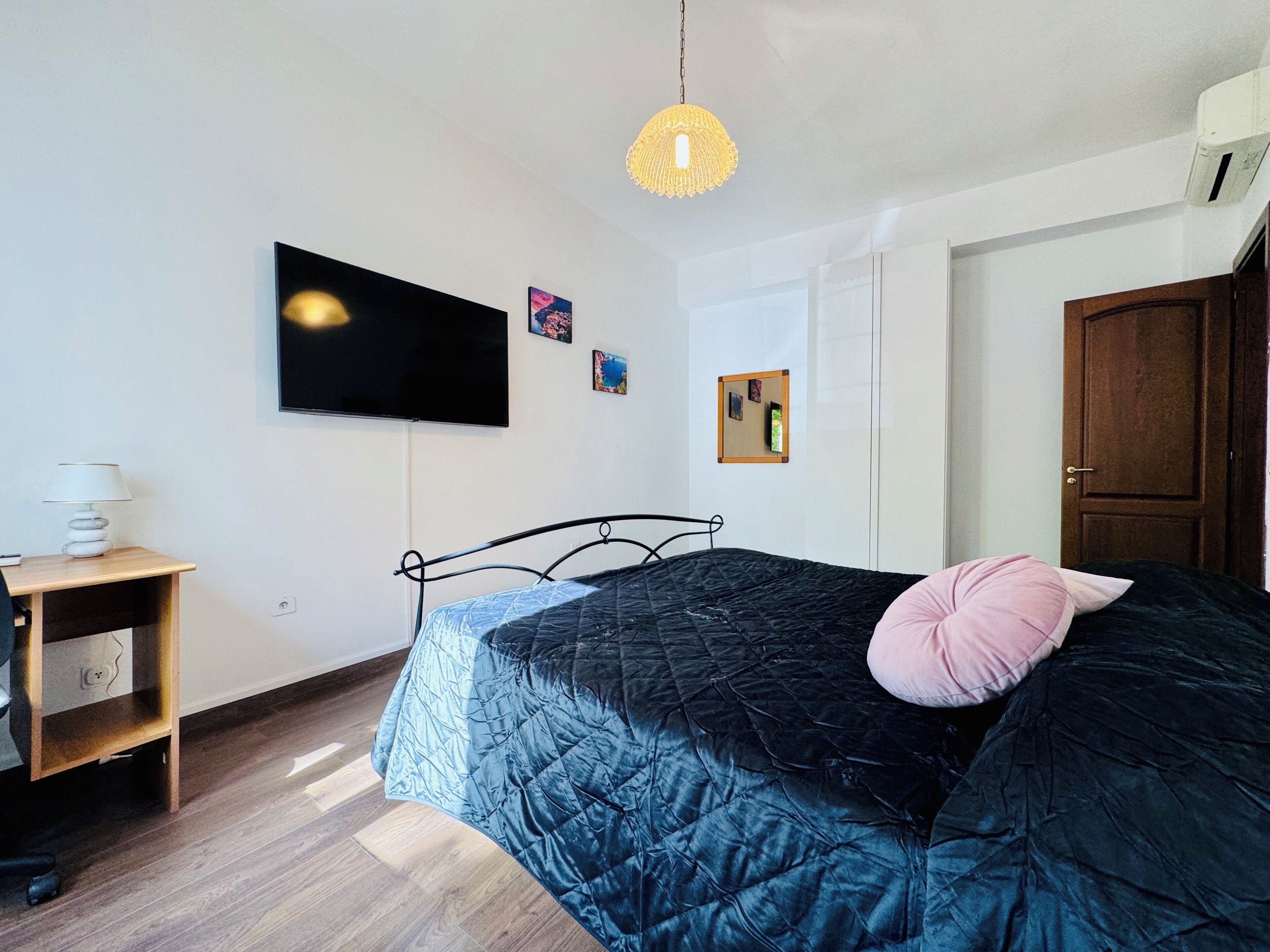Un dormitorio con cama, televisor, escritorio y puerta.