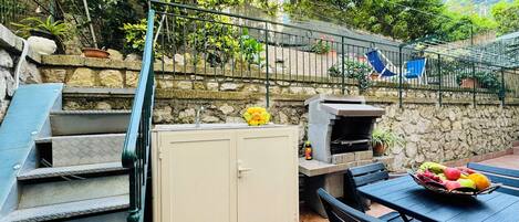 Un espace patio agrémenté d’un mur en pierre, d’un barbecue, d’un évier et d’une table sur laquelle sont disposés des fruits.
