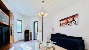 A living room with a TV, fireplace, sofa, glass coffee table, and a chandelier. - YourHome - Letizia's House (Sorrento)
