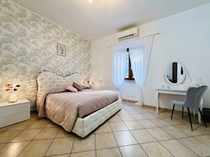 Ein Schlafzimmer mit Bett, Nachttisch, Lampe, Spiegel und einem Fenster mit Vorhängen.