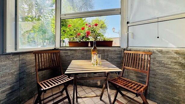 A corner table with two wooden chairs, a bottle, and a glass, with a window view of greenery and a potted plant. - YourHome - Letizia's House (Sorrento)