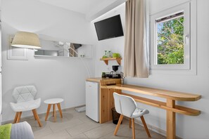 A modern kitchen with a wooden countertop, white chairs, a small refrigerator, a TV mounted above the counter, and a window with a view of trees. - Studio Apartment 'Sivota Colours 25' with Private Terrace, Wi-Fi and Air Conditioning (Sivota)