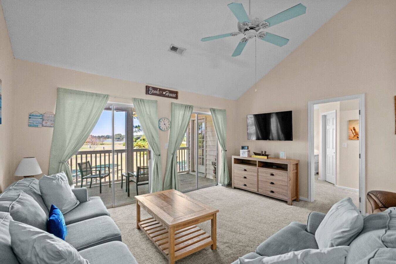 A living room with a sofa, a coffee table, a TV, and a balcony with curtains.