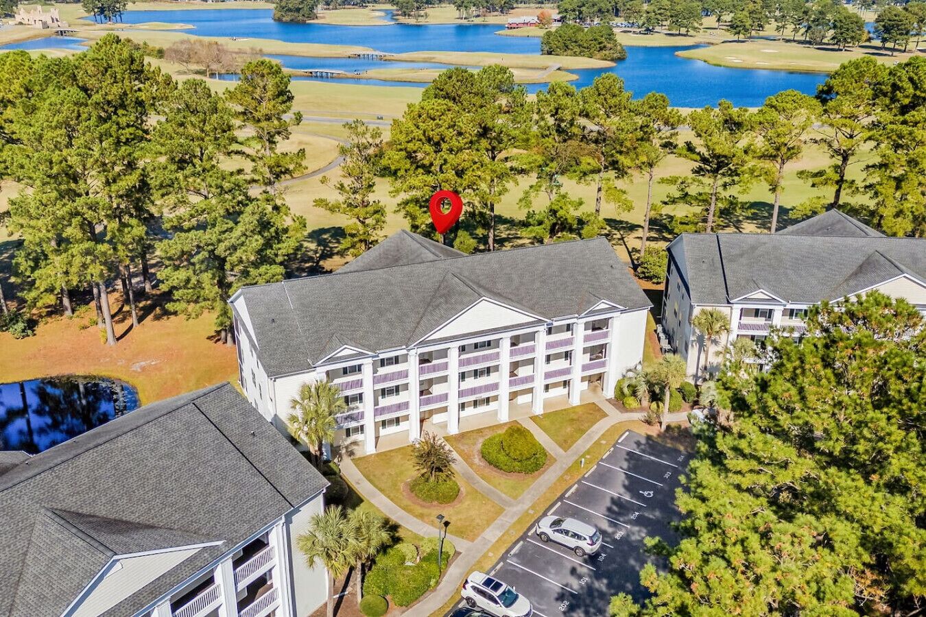 A multi-story hotel with a central courtyard, parking lot, and views of a golf course and lakes.