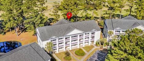 A multi-story hotel with a central courtyard, parking lot, and views of a golf course and lakes.