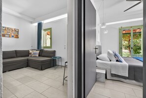 A modern living room with a sectional sofa, a small table, and a bed with a green window frame. - Apartment 'Sivota Colours 42' with Private Terrace, Wi-Fi and Air Conditioning (Sivota)