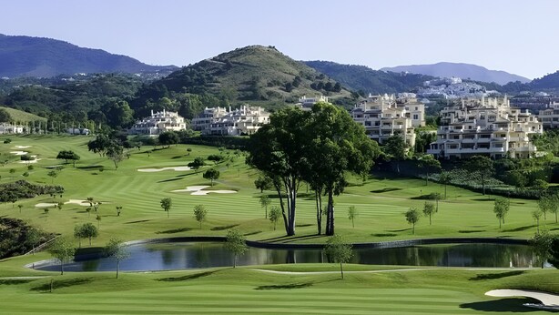 Un campo de golf con búnkeres, un estanque y edificios residenciales al fondo.