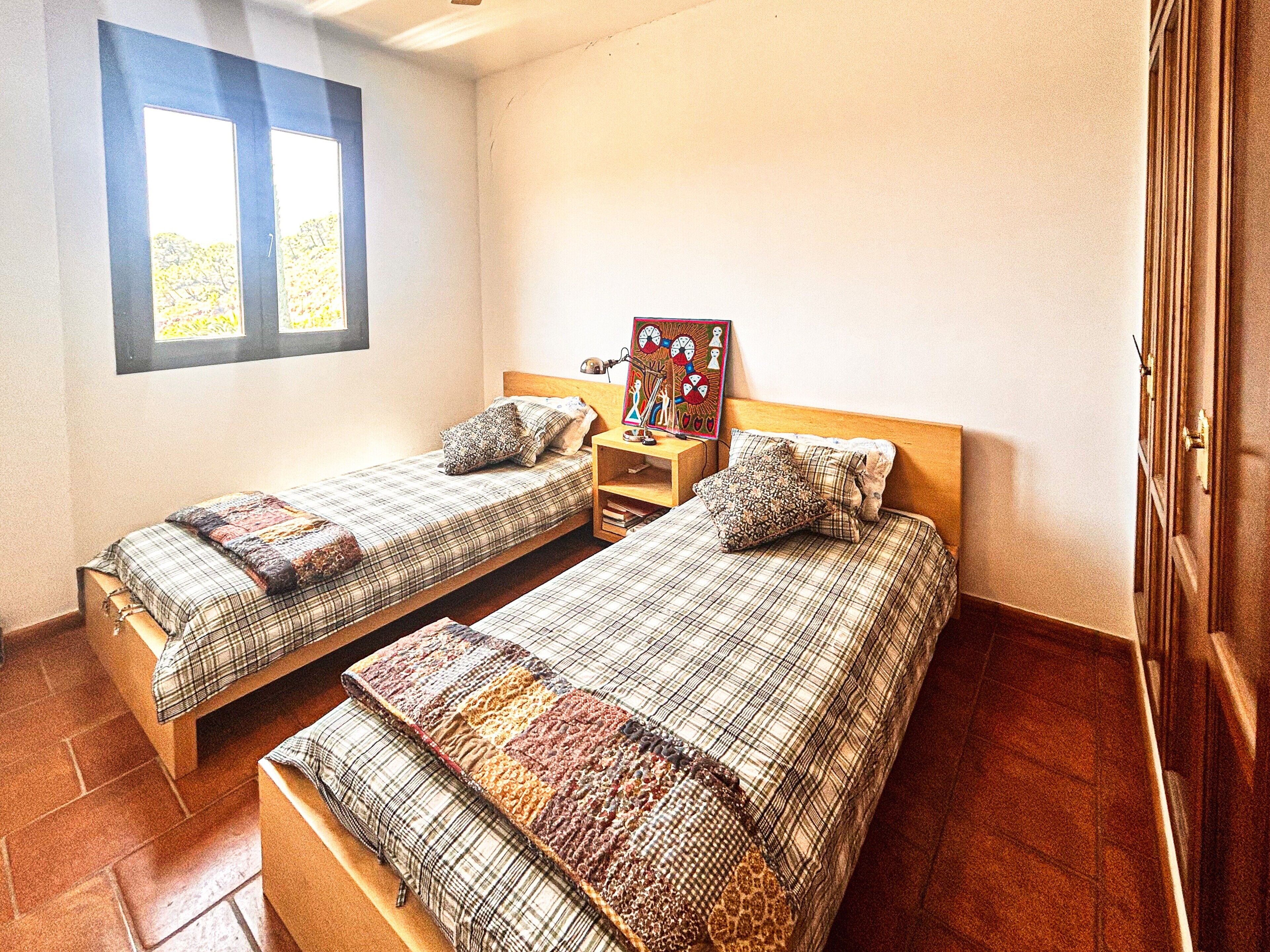 A room with two beds, a nightstand, a painting, and a window.