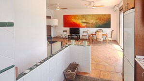 Una cocina moderna con armarios blancos, un comedor con un cuadro grande y un ventilador de techo.